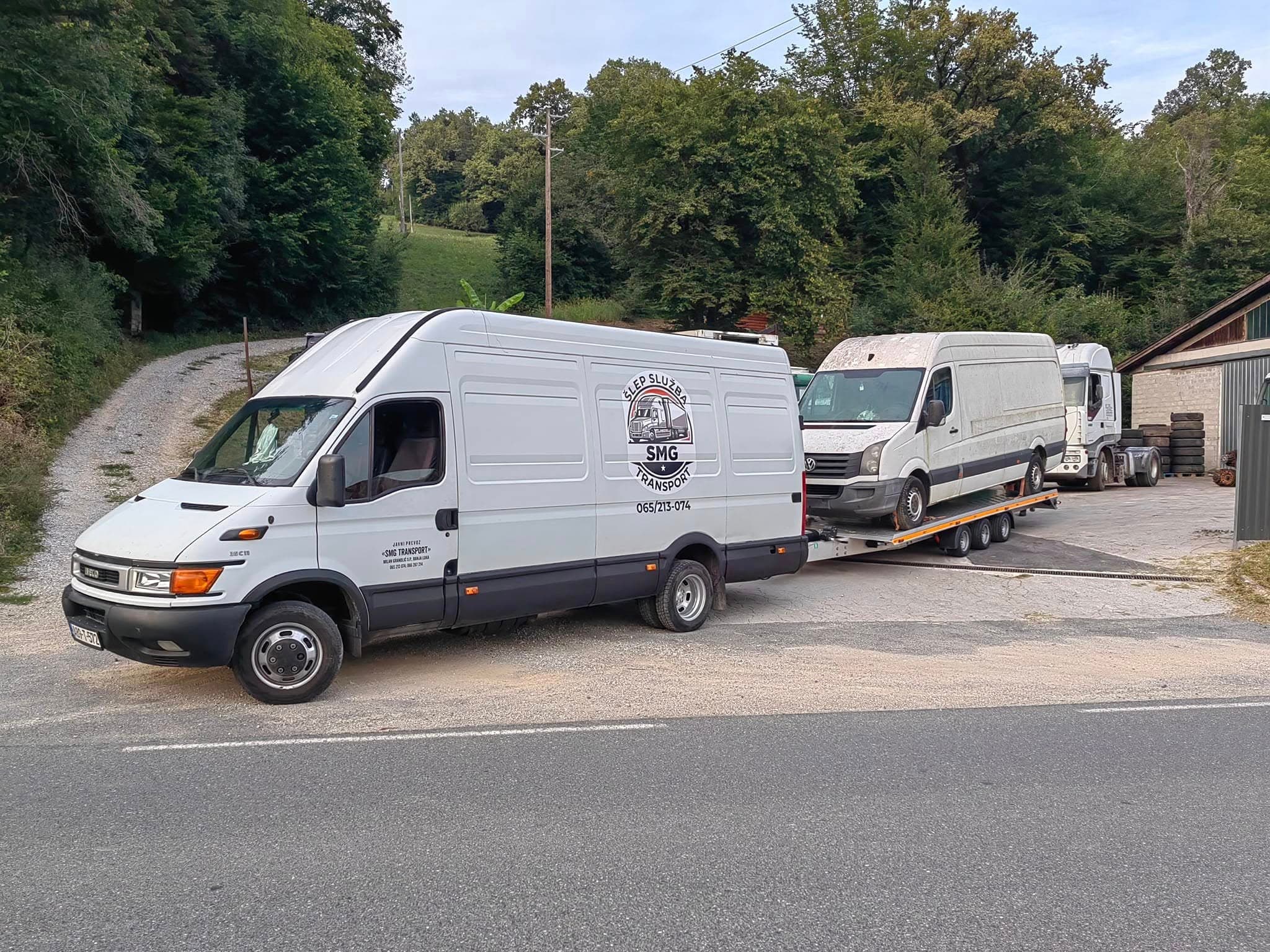 Bijeli kombi SMG Transport vuče prikolicu na kojoj se prevozi drugi kombi