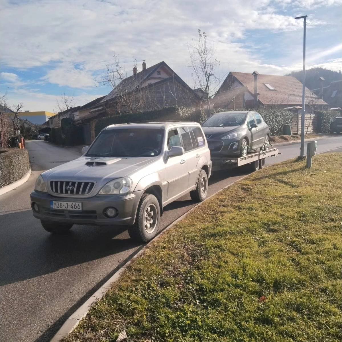 Terensko vozilo SMG Transport vuče prikolicu sa automobilom kroz naselje