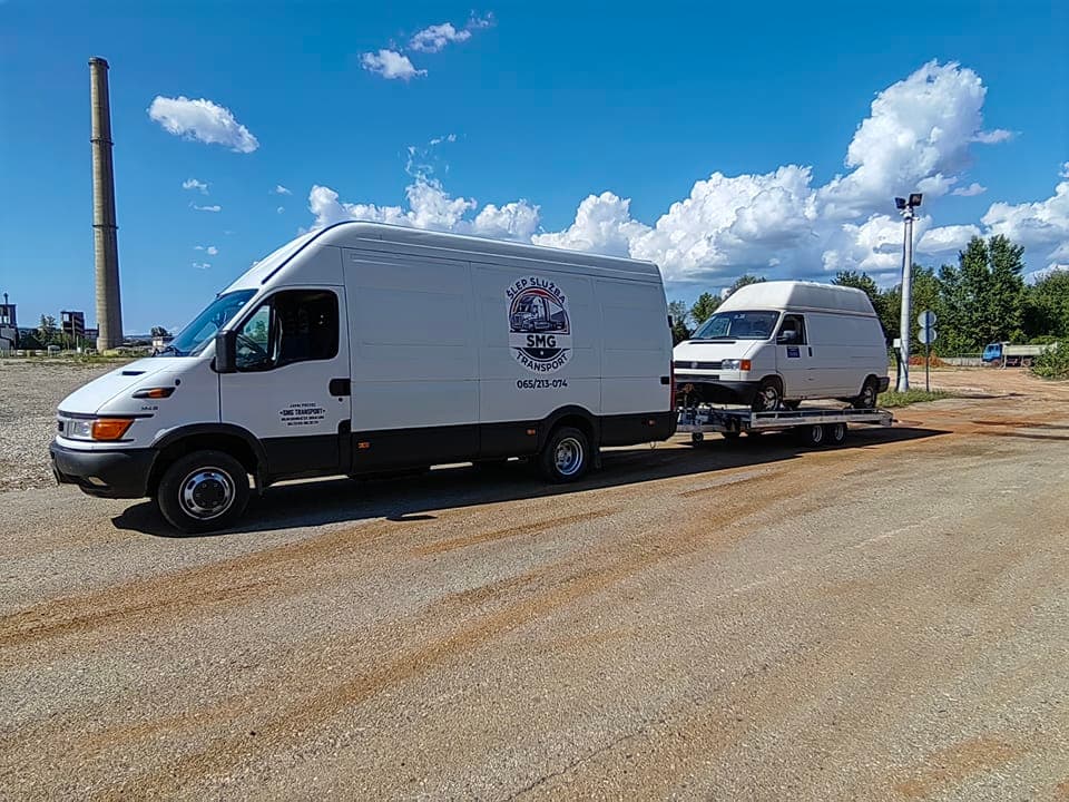 Kombi SMG Transport sa prikolicom na kojoj prevozi drugi kombi, pod vedrim nebom